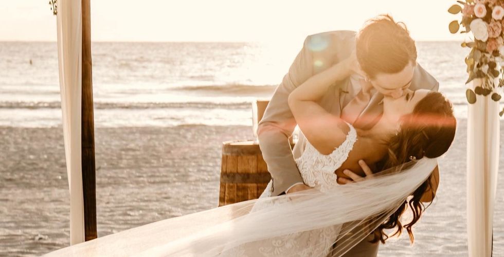 A Man And Woman Sitting On A Bench In Front Of A Beach